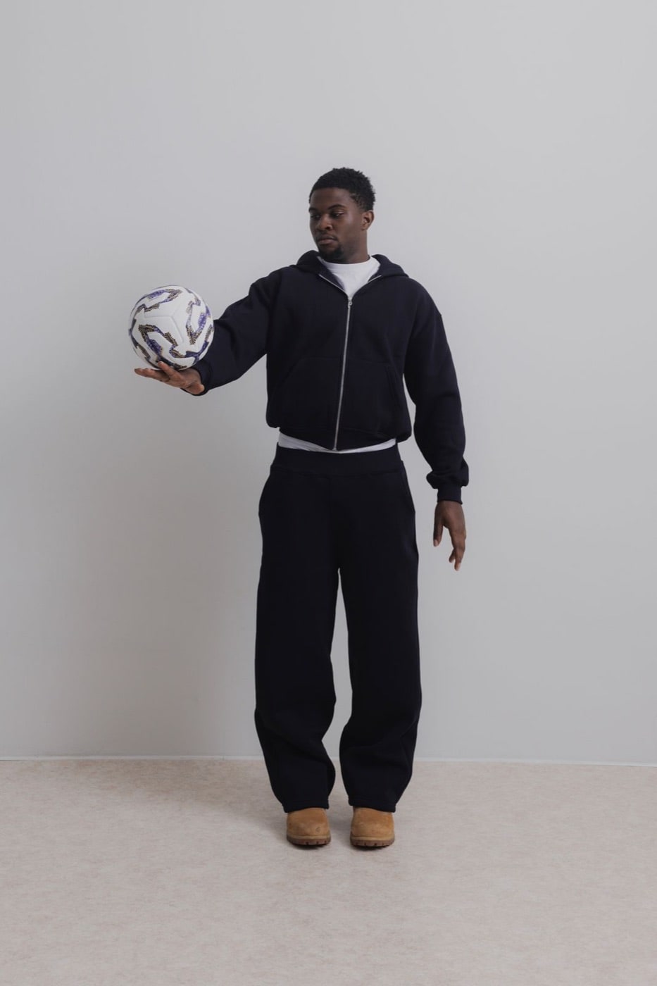 Modello con la zip hoodie della capsule PERFECT × Virtus Verona e un pallone